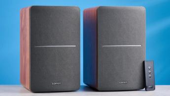 Die Edifier R1280T Regallautsprecher in Holzoptik vor blauem Hintergrund, mit sichtbaren Lautstärkereglern, Treibern, Hochtönern, RCA- und AUX-Eingängen sowie Fernbedienung.