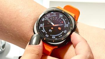Nærbillede af Samsung Galaxy Watch Ultra med en kraftig orange rem og analog urskive på en brugers håndled