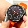 Nærbillede af Samsung Galaxy Watch Ultra med en kraftig orange rem og analog urskive på en brugers håndled
