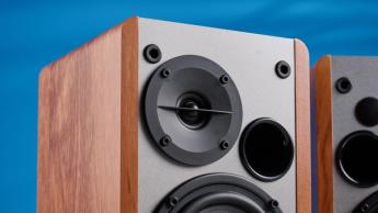 Die Edifier R1280T Regallautsprecher in brauner Holzoptik vor blauem Hintergrund, mit sichtbaren Lautstärkereglern, Lautsprechertreibern, Hochtönern, RCA- und AUX-Eingängen sowie Fernbedienung.