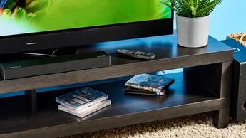 Die Ultimea Nova S50, eine schwarze kompakte Soundbar mit Front-LED und kabelgebundenem Subwoofer, an einer TV-Halterung mit einem Panasonic-TV verbunden