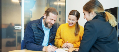 Foto av mann og kvinne som signerer et salgsoppdrag mens megleren ser på.