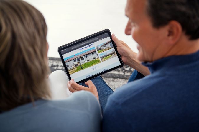 Par sitter med ryggen til kamera og ser på en eiendom på en tablet. Foto.