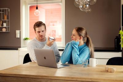 Foto av mann og kvinne som sitter ved et bord, snakker i telefon og har en Mac på bordet. Begge ser bekymret ut.