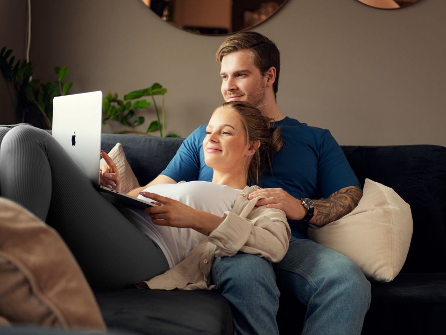 Ungt par i sofa ser på en mac-skjerm sammen. Foto