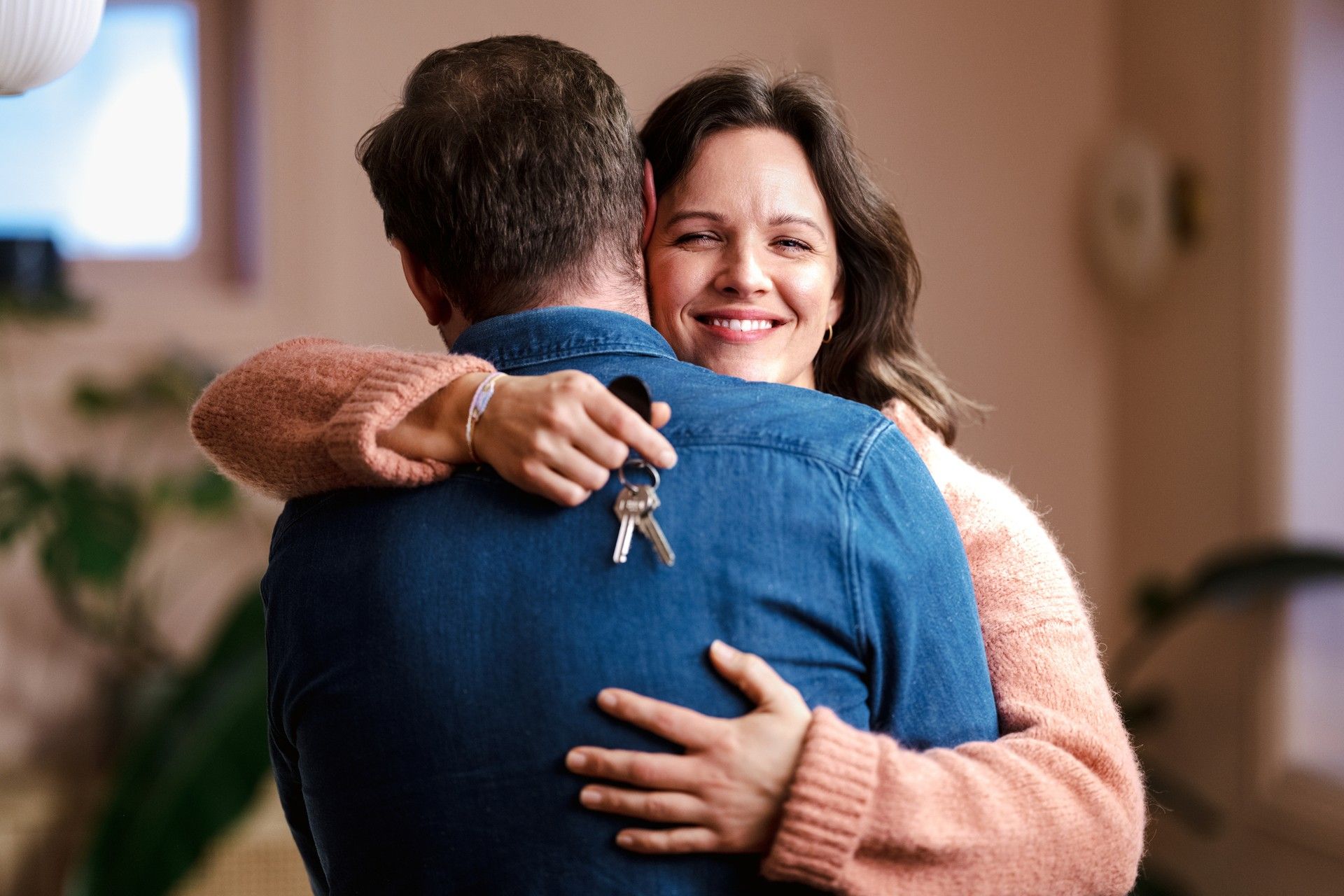 Foto av smilende kvinne vendt mot kamera, som klemmer en mann med ryggen mot kamera. Kvinnen holder et nøkkelknippe.
