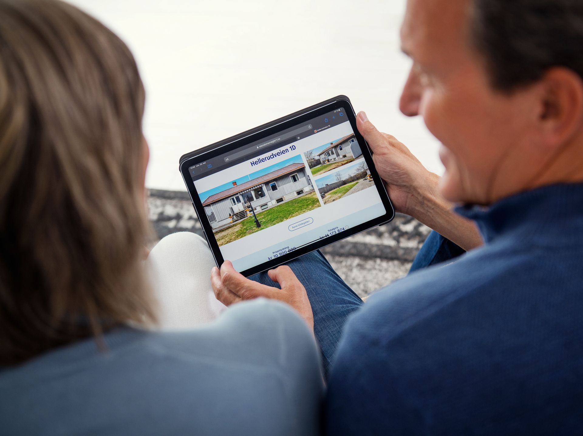 Par sitter med ryggen til kamera og ser på en eiendom på en tablet. Foto.