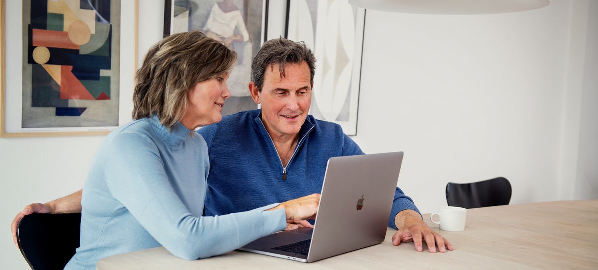 Par sitter sammen ved et bord og ser på en pc-skjerm. Foto.