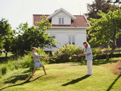 Jente og gutt spiller badminton. Hytte i bakgrunnen. Foto.