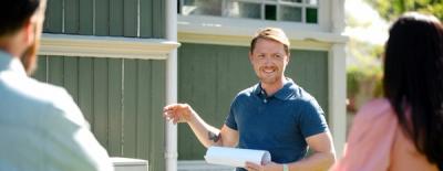 Foto av en fagmann som står foran et stort, grønt hus. Han snakker med en mann og en kvinne som står med ryggen til i forgrunnen.