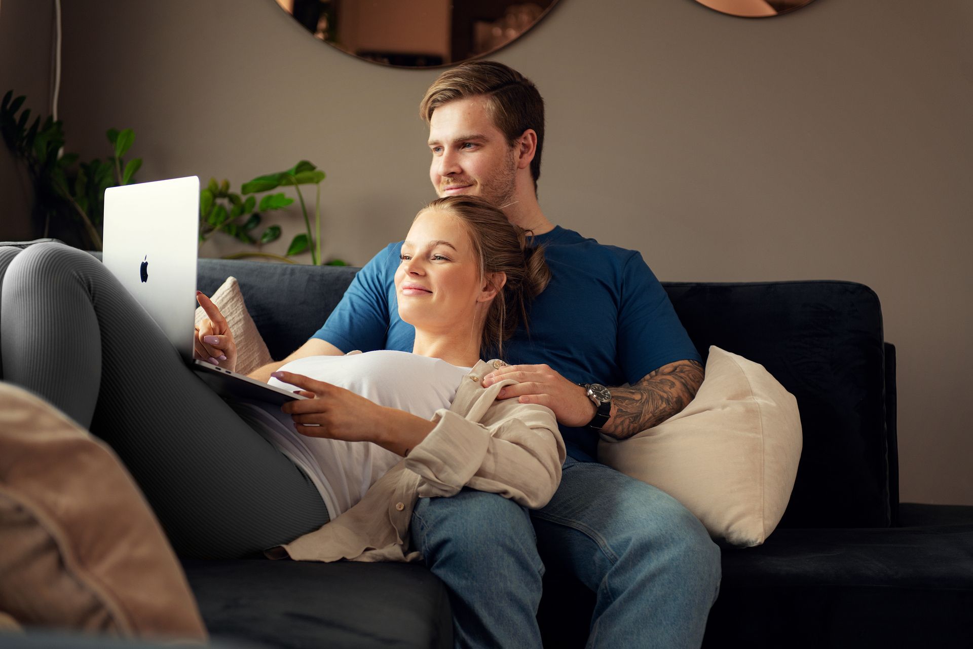 Foto av ungt par i sofa som sitter tett sammen og ser på en Mac-skjerm sammen