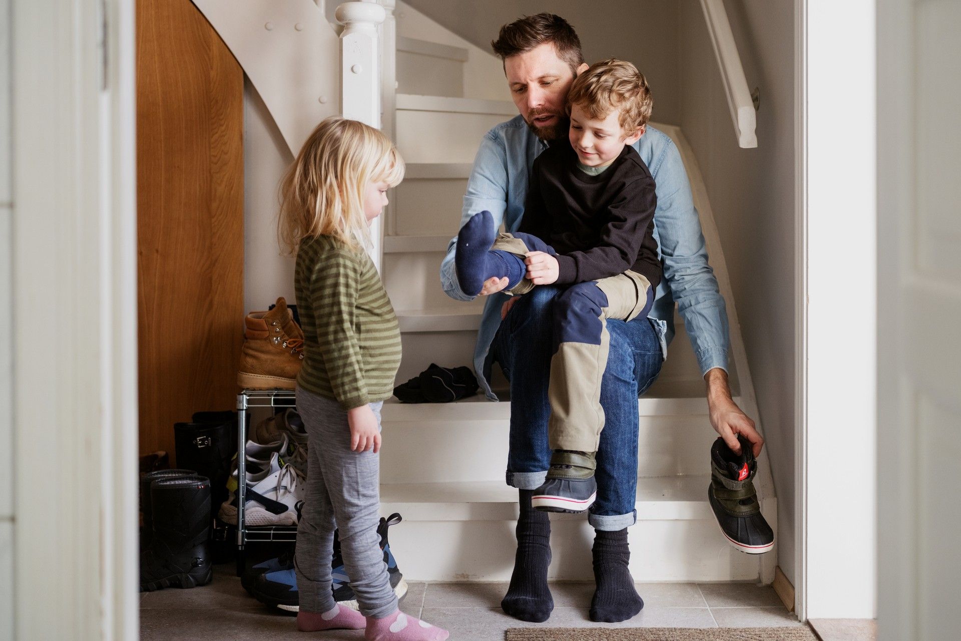 Foto av pappa som sitter i en trapp med et barn på fanget. ved siden av står et barn til og ser på dem.