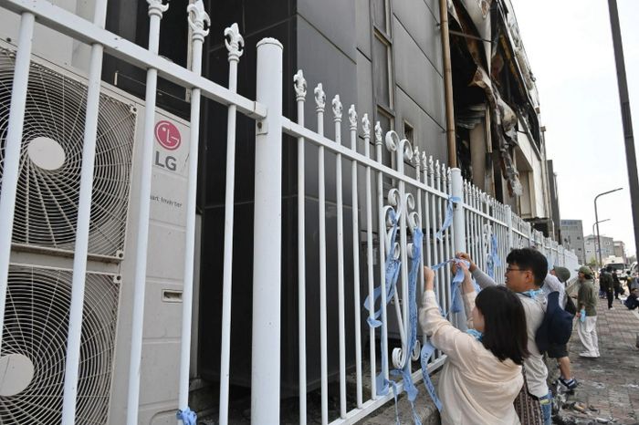 불에 탄 아리셀 공장 담장에 추모 리본을 달고 있는 참가자들. 