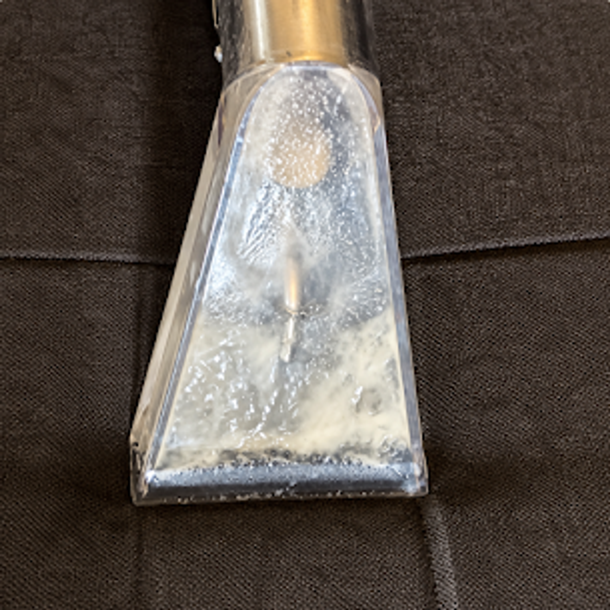 Close view of an upholstery extraction tool recovering moisture from sofa fabric.