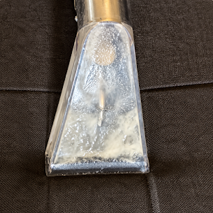 Close view of an upholstery extraction tool recovering moisture from sofa fabric.