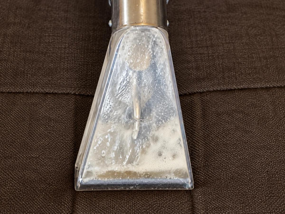 Close view of moisture and foam being recovered through a transparent upholstery extraction tool.