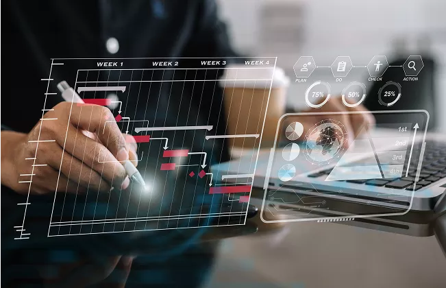 Person verwendet einen Stylus auf einem Tablet mit einem digitalen Gantt-Diagramm und Analyse-Interface, im Hintergrund sind ein Laptop und ein Kaffeebecher zu sehen.