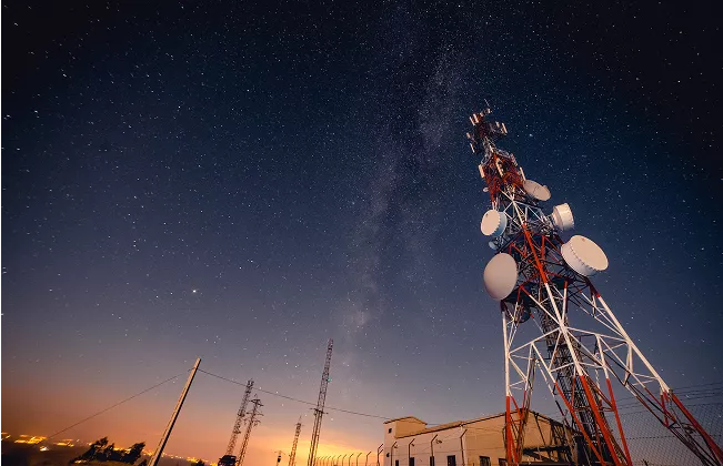 Telecommunication tower with multiple antennas under a starry night sky, with the Milky Way visible in the background.
