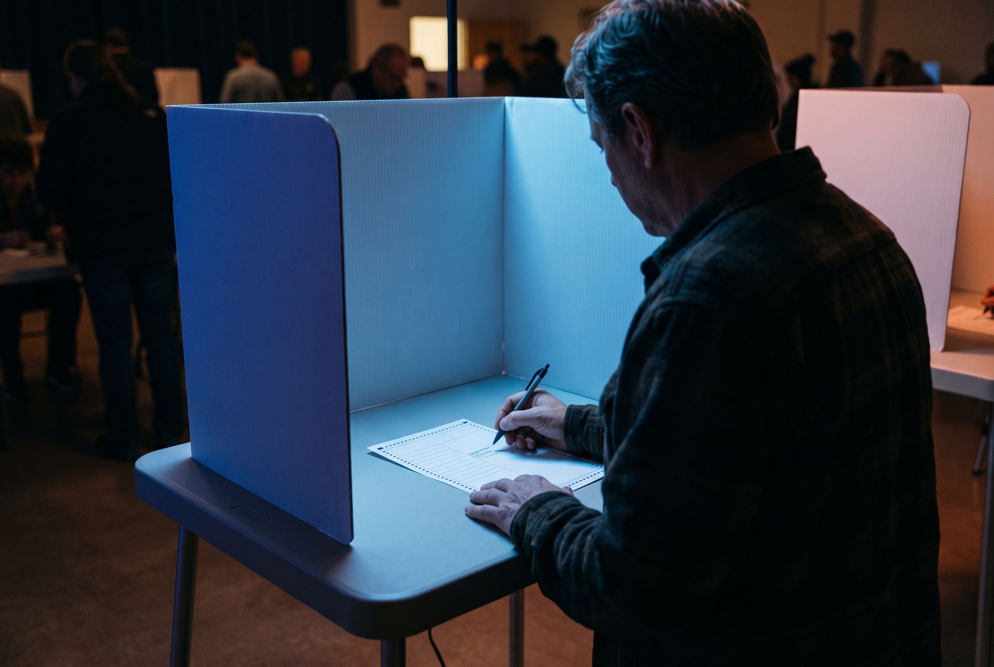 Man voting at a voting booth with a blue light cast on him