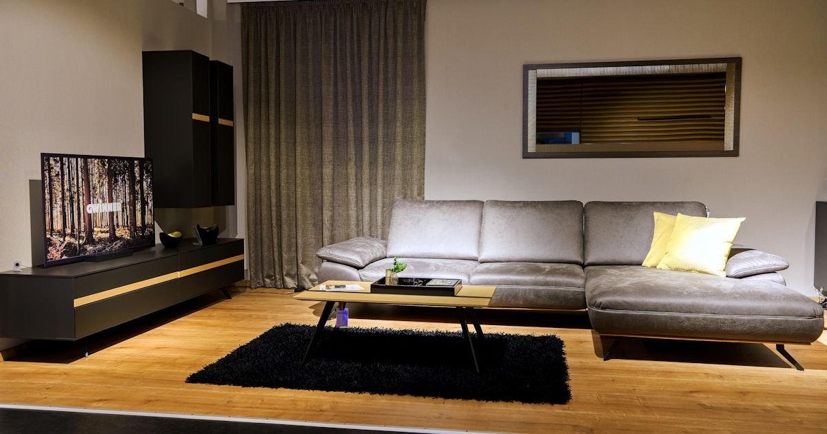 Grey sectional sofa with yellow cushions beside a black TV wall unit and coffee table on wood flooring.