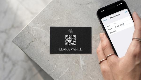 A matte-black business card with a white QR code on it next to an iPhone showing the iOS ‘Add to Contacts’ sheet