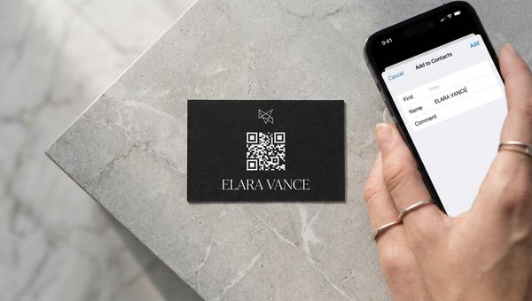 A matte-black business card with a white QR code on it next to an iPhone showing the iOS ‘Add to Contacts’ sheet