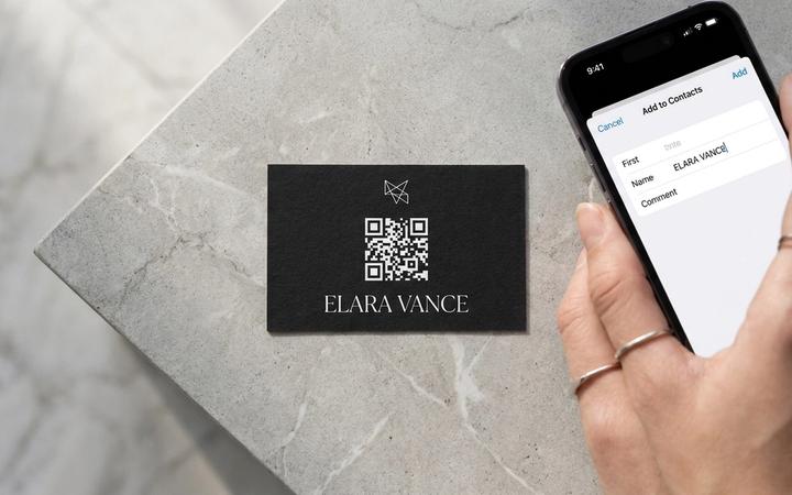 A matte-black business card with a white QR code on it next to an iPhone showing the iOS ‘Add to Contacts’ sheet