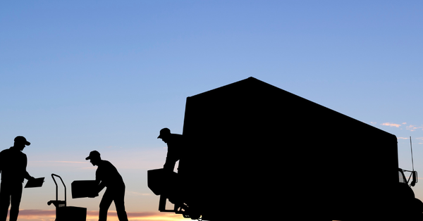 silhouettes of people moving boxes out of a truck early in the morning