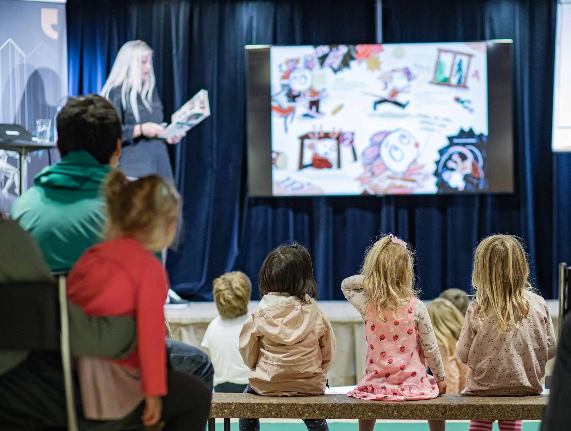 Barn sitter på benk og hører på forfatter på Søndagsbarn.