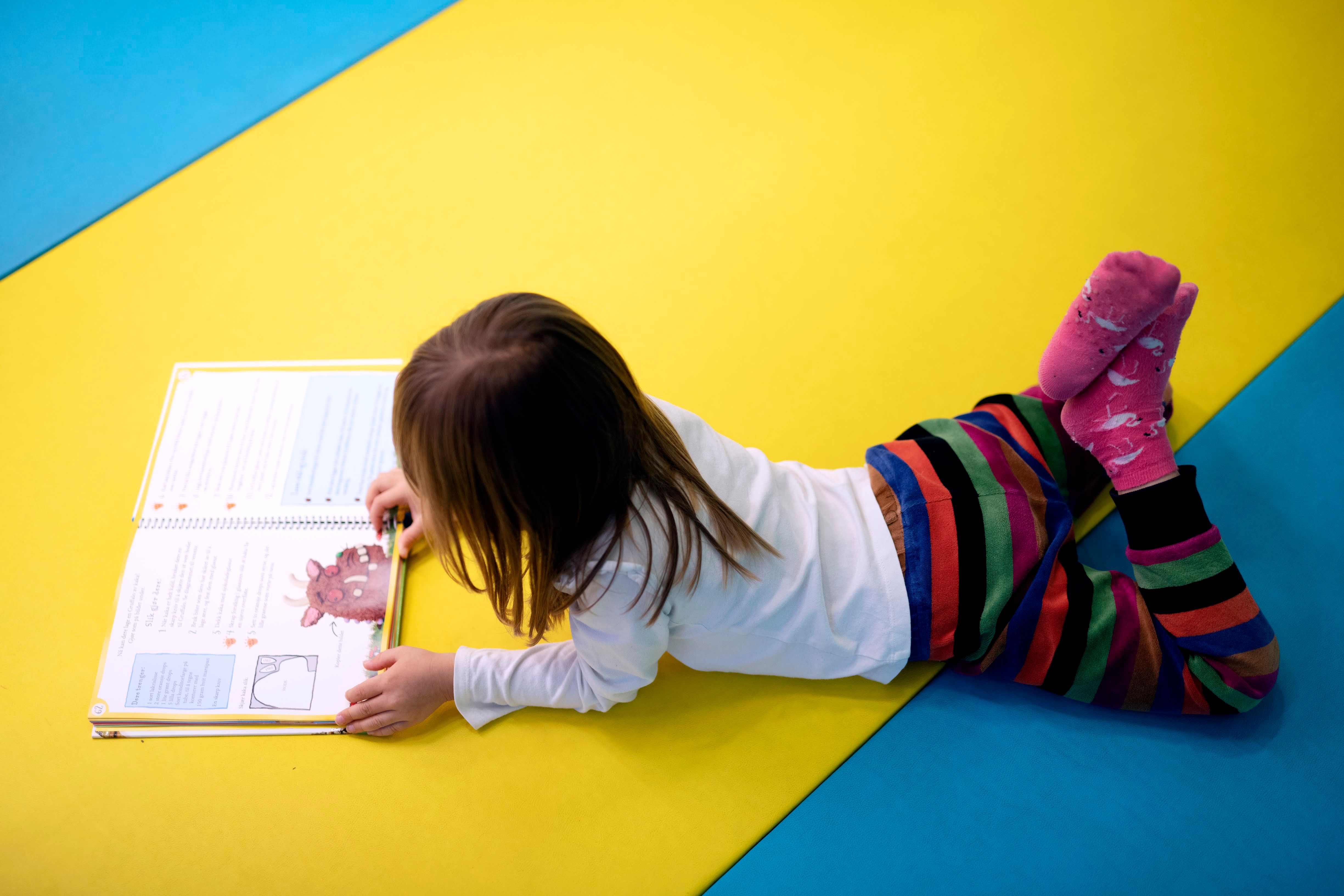 Jente ligger på gulvet og leser en bok
