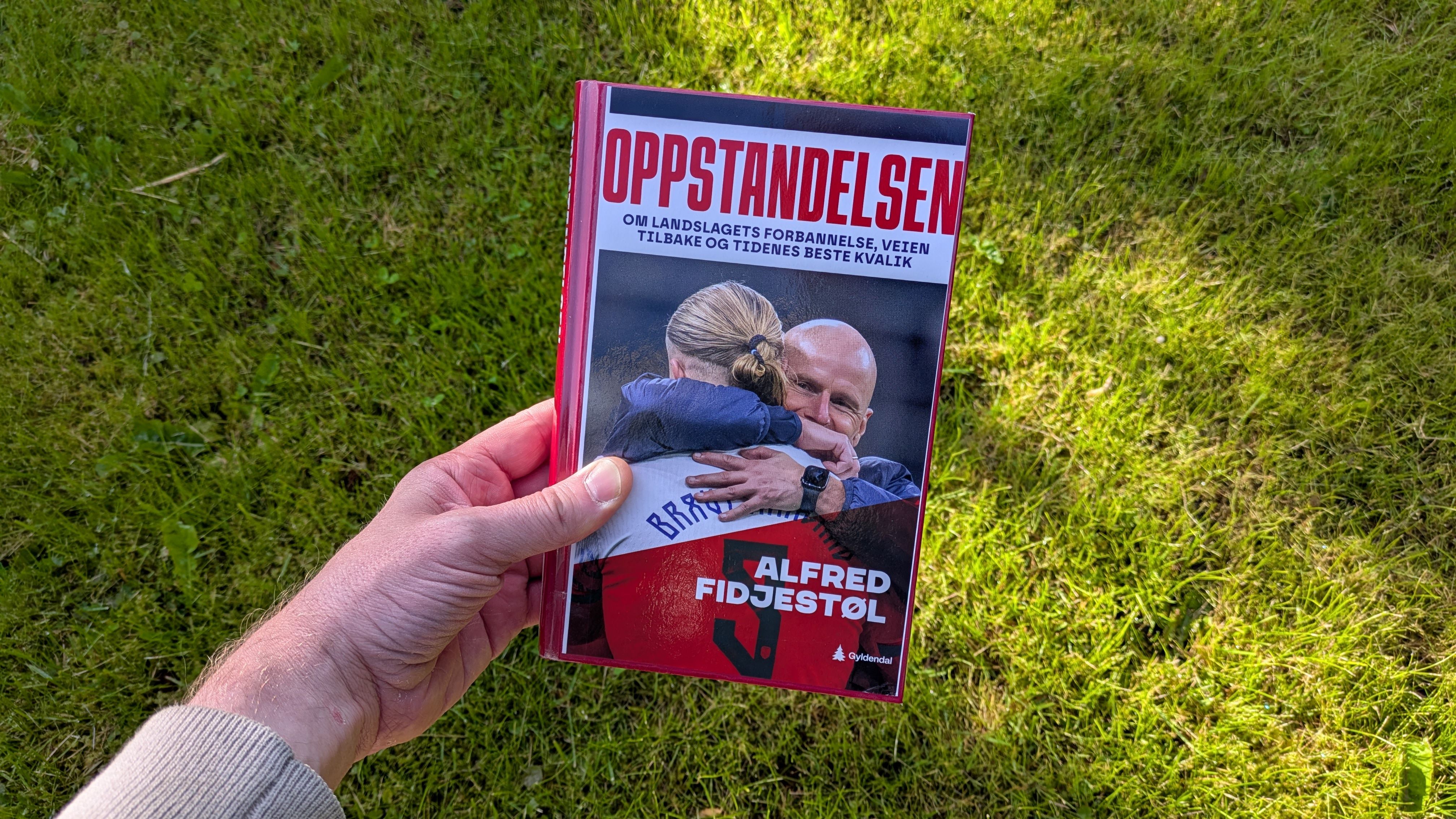 Boka Oppstandelsen av Alfred Fidjestøl holdt foran en gressplen
