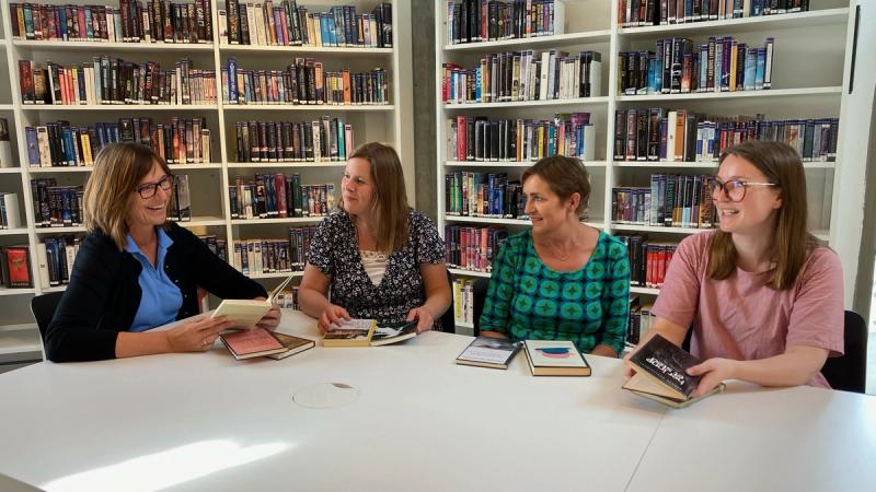 Fire bibliotekarer med bok ved bord