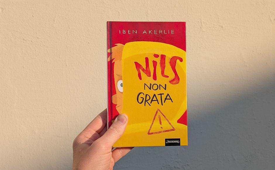 Nils non grata av Iben Akerlie holdt foran en vegg med sol