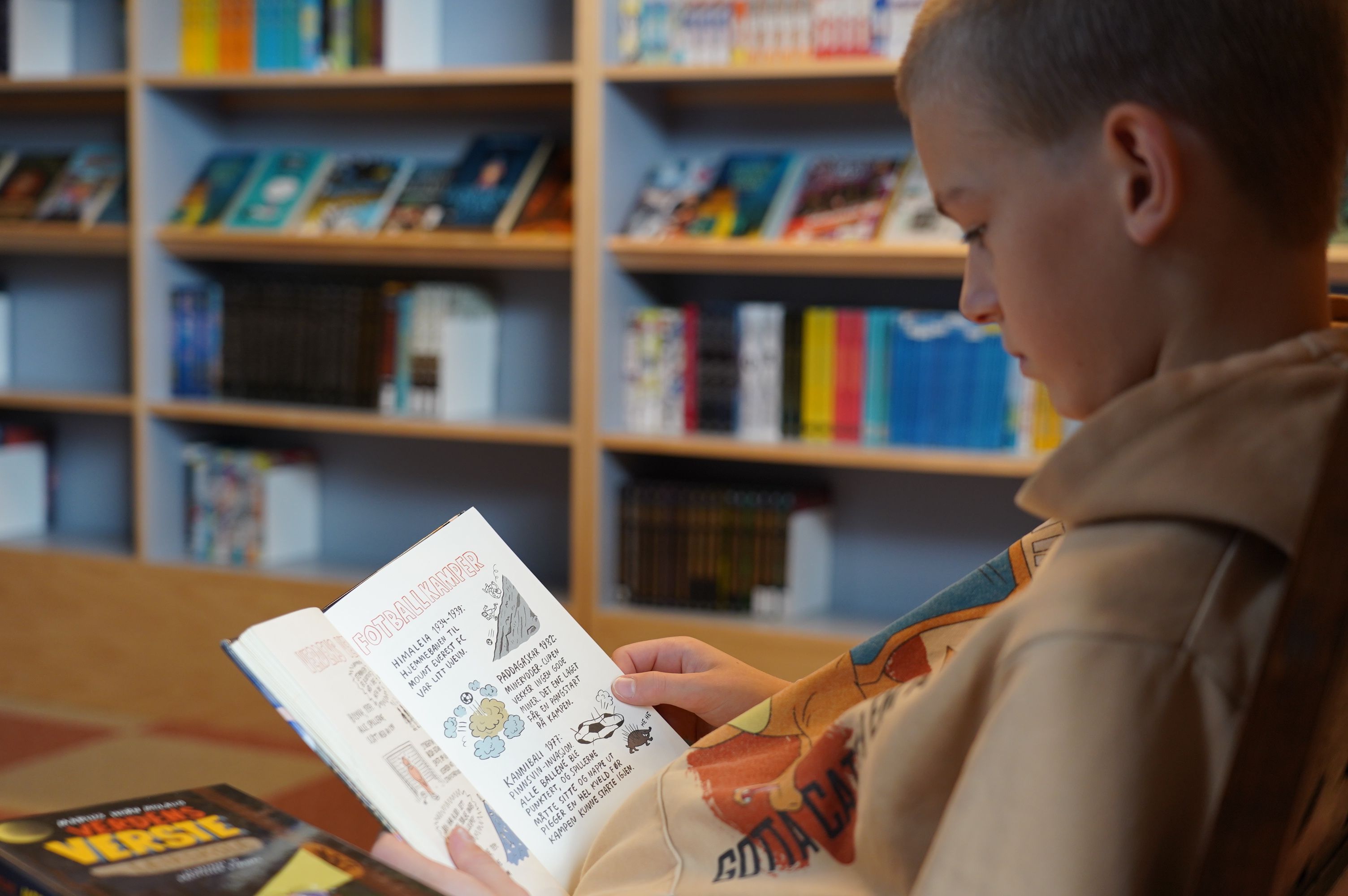 Gutt leser bok på biblioteket
