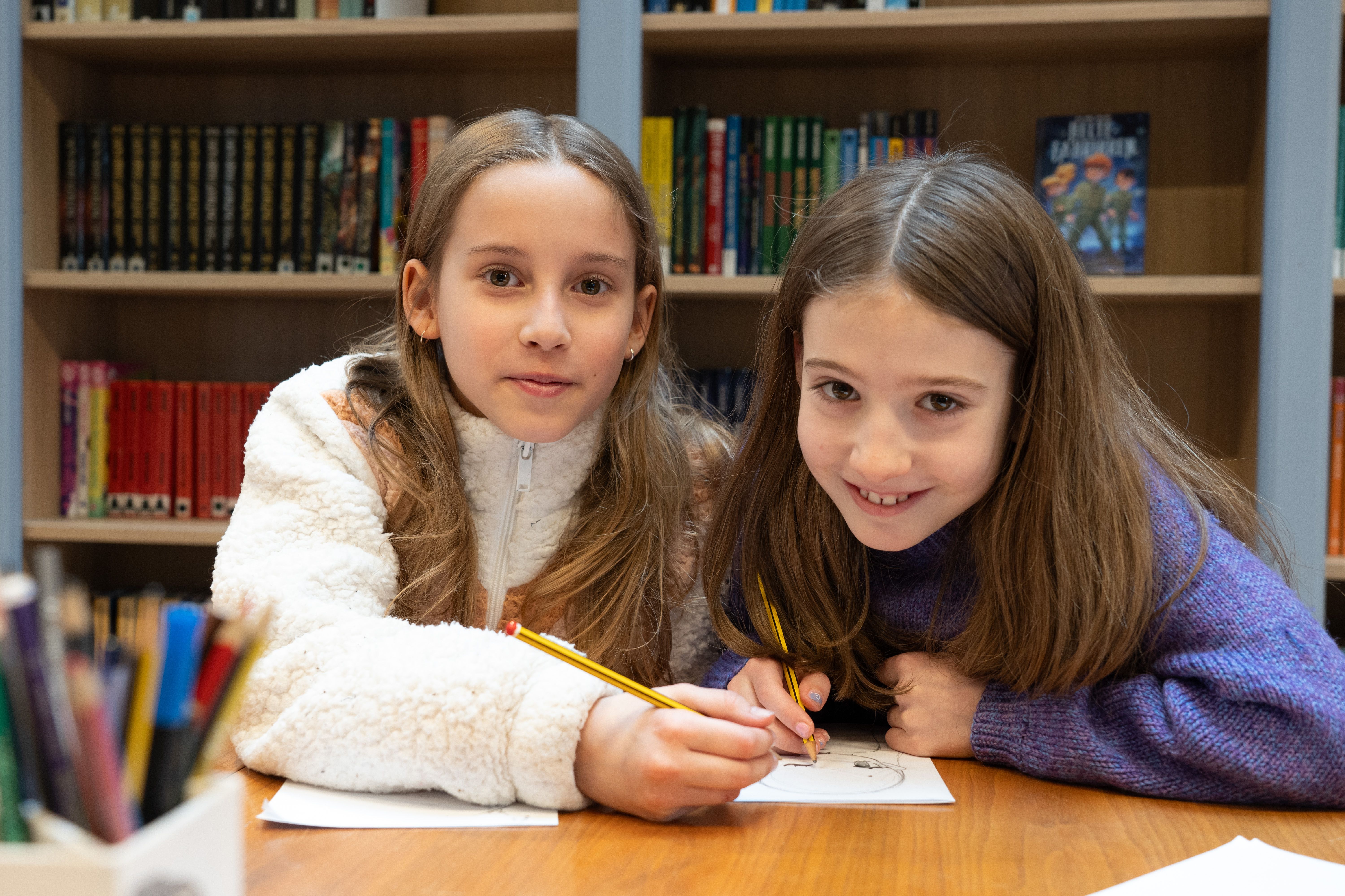 Bilde av to jenter skriver fortellinger i biblioteket. 