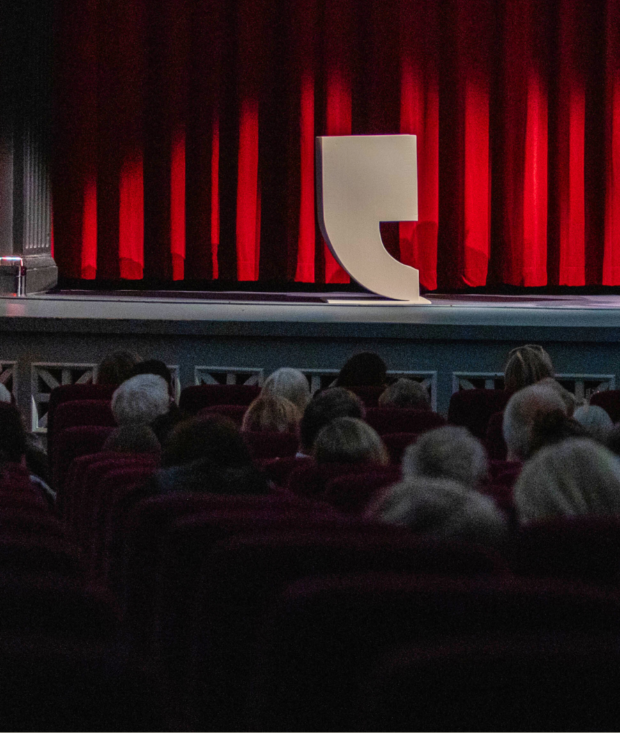 Kapittel-logo stående på en scene med rødt sceneteppe bak