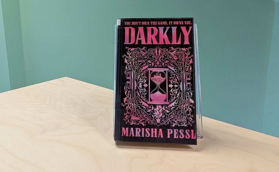 Boka Darkly stående på en bokhylle foran en grønn vegg