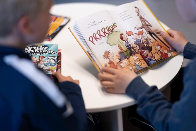 Barn som leser i bildebok, hender som holder bok