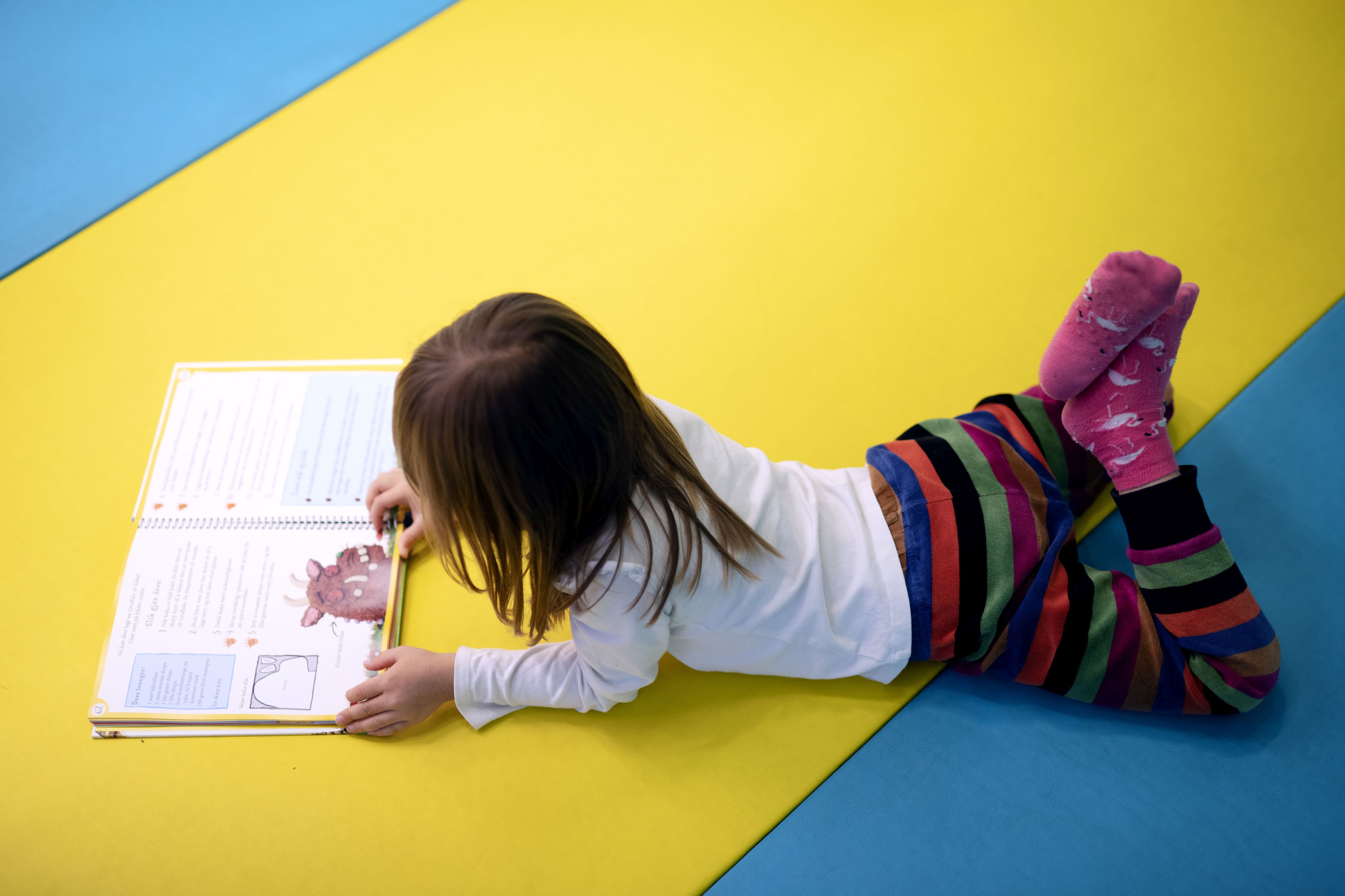 Jente ligger på gulvet i biblioteket og leser.
