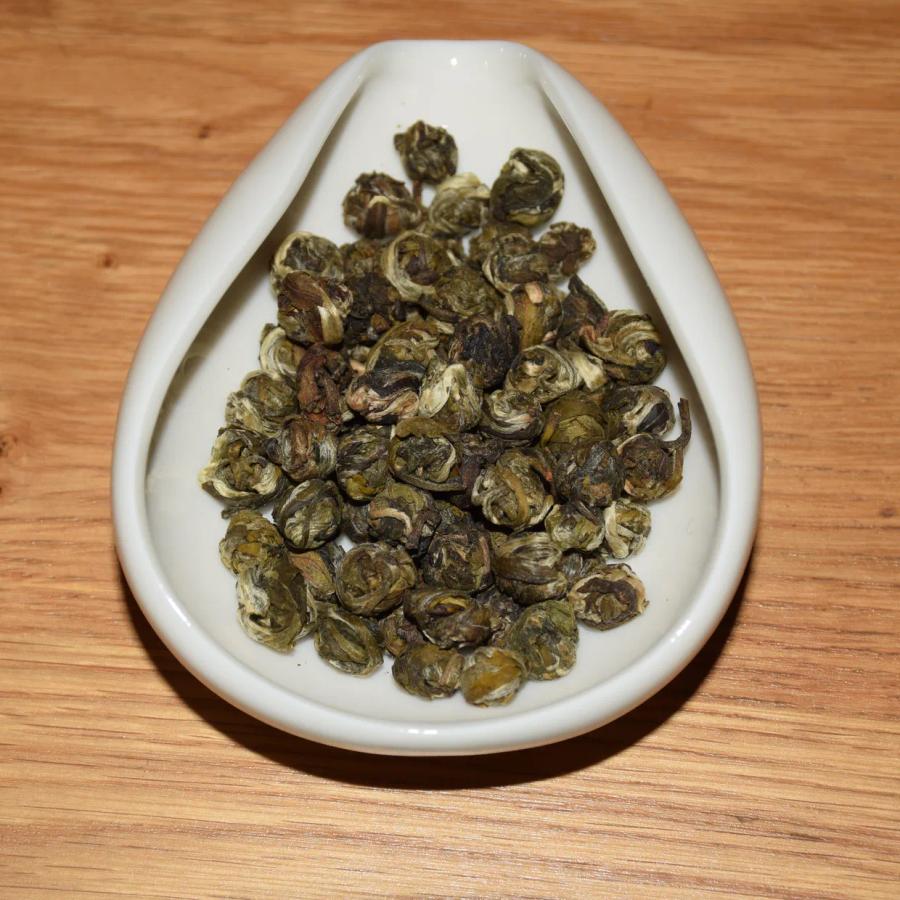 Premium Jasmine Dragon Pearl green tea for global bulk sourcing, displaying tightly hand-rolled tea pearls in a white ceramic dish on a wooden surface.