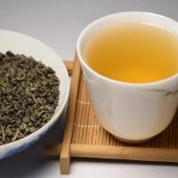 Professional tasting display of wholesale organic Gunpowder green tea, showcasing tightly rolled dry pellets alongside a clear, bright yellow-green liquor.