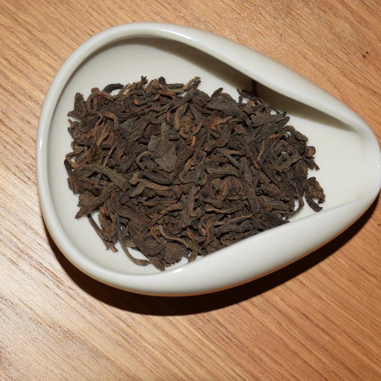 Dry leaf of loose ripe pu-erh, shown in a white porcelain scoop on a wooden table