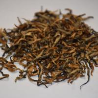 Quality inspection of wholesale Shaoguan Honey Black Tea, showing tightly twisted loose leaves and abundant golden tips on a white plate.