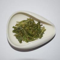 Macro close-up of authentic Xinchang Da Fo Dragon Well dry tea leaves, perfectly presented in a teardrop-shaped white ceramic scoop.