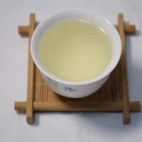 Close-up of freshly brewed Dongting Biluochun green tea in a white ceramic cup on a bamboo coaster.
