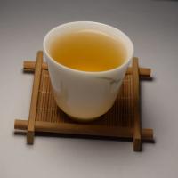 Professional tasting of wholesale organic Gunpowder green tea, showcasing a clear and bright golden-green liquor in a white ceramic cup.