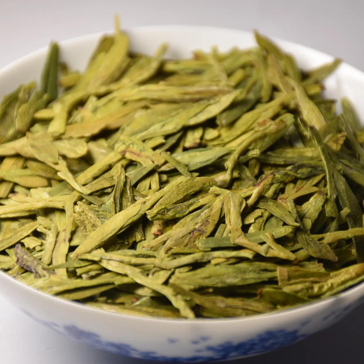 Flat, sword-shaped Longjing green tea leaves in a blue-and-white porcelain bowl