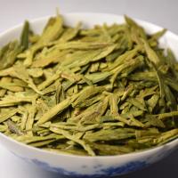 Premium West Lake Dragon Well (Longjing) dry green tea leaves served in a traditional blue and white porcelain bowl.