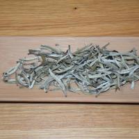 Close-up of authentic Guangxi Silver Needle white tea leaves spread on a light wooden tray, highlighting their natural greenish-white color.