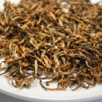 Close-up of premium Shaoguan Honey Black Tea dry leaves, showing abundant golden tips on a white plate.